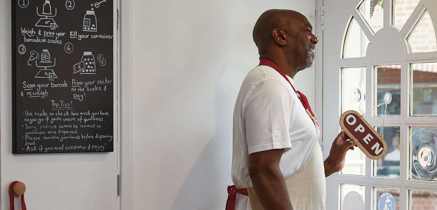 Man smiling wearing an apron putting 'open' sign on a shop door Man smiling wearing an apron putting 'open' sign on a shop door