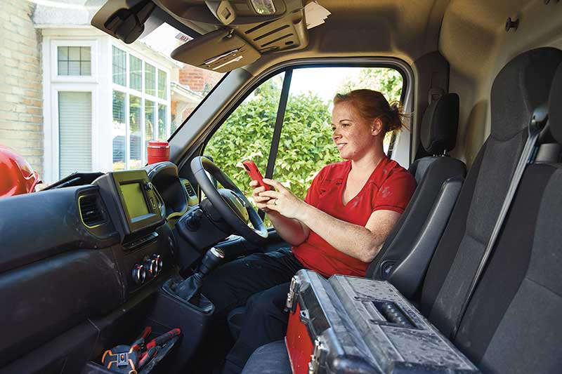 Person sitting in rhe drivers seat of a van beside a toolbox holding a phone parked in front of a house Person sitting in rhe drivers seat of a van beside a toolbox holding a phone parked in front of a house