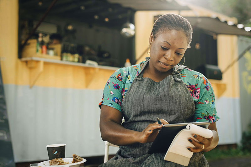 Person standing in front of a food stand holding a tablet and roll of paper Person standing in front of a food stand holding a tablet and roll of paper