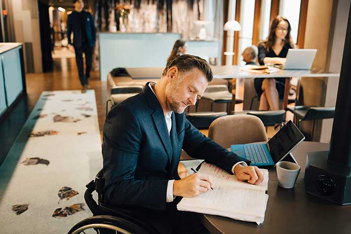 Person sitting at desk in co-working space with a laptop, writing in a notebook Person sitting at desk in co-working space with a laptop, writing in a notebook