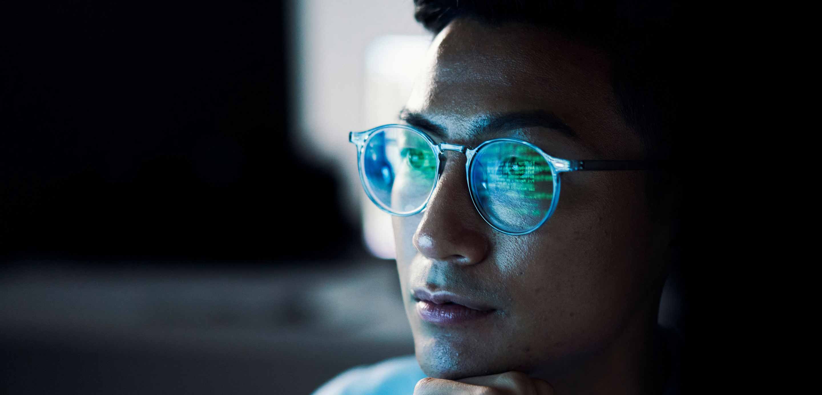 Man viewing computer screen with data reflecting in his glasses.