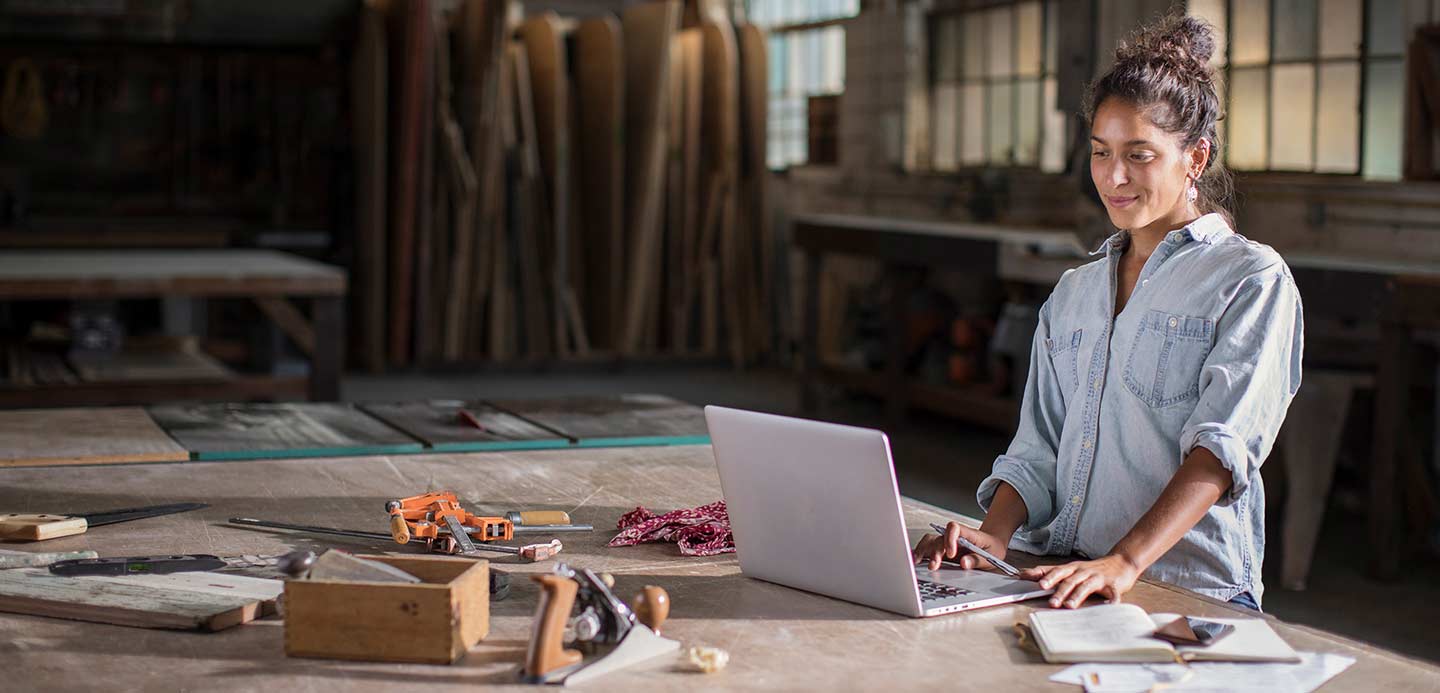 Person smiling sitting at a work bench covered in tools on laptop Person smiling sitting at a work bench covered in tools on laptop