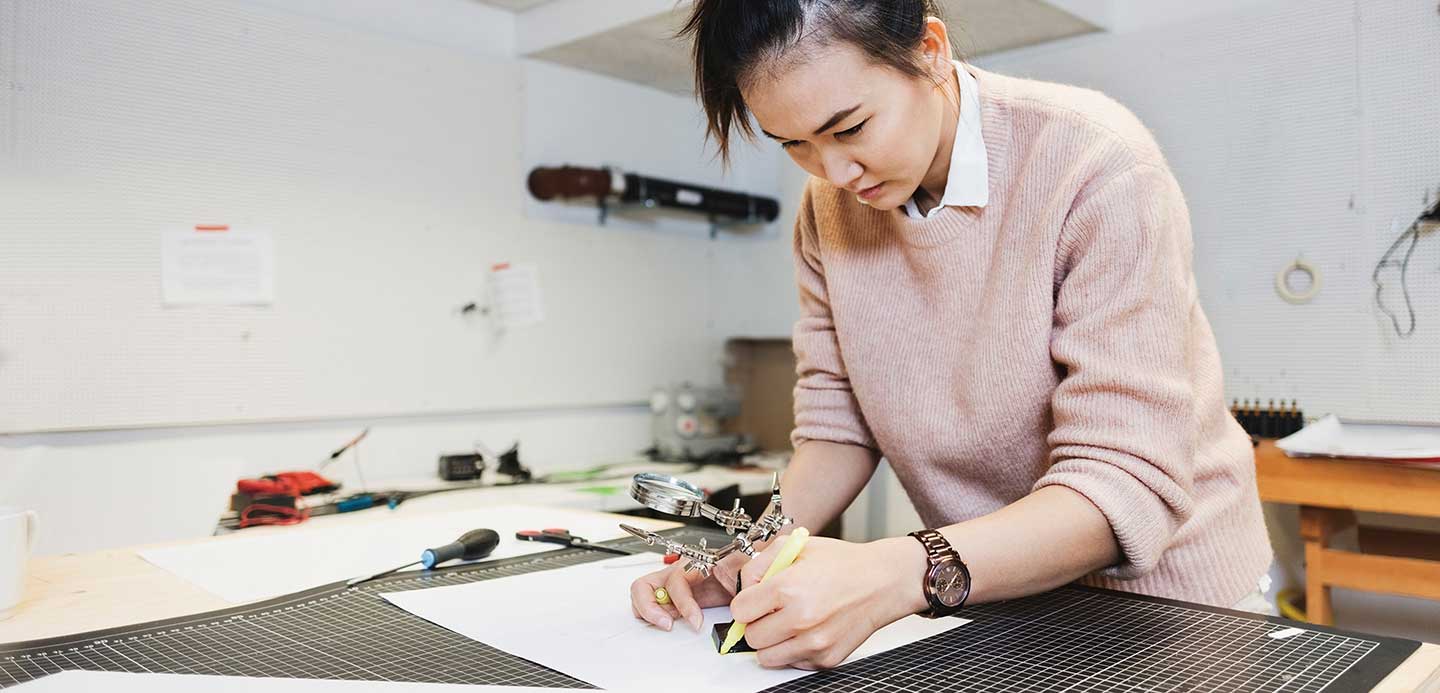 Woman in workshop with tools in the background drawing on a piece of paper Woman in workshop with tools in the background drawing on a piece of paper