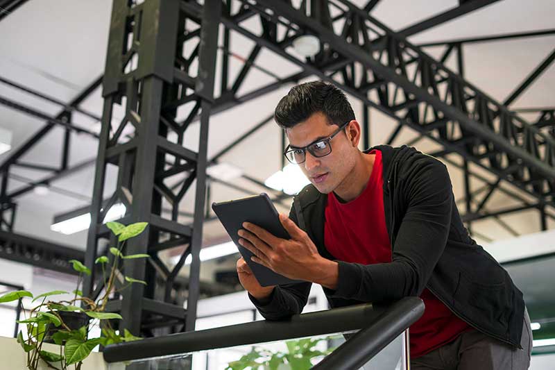 Person holding a tablet leaning against a railing in an office space Person holding a tablet leaning against a railing in an office space
