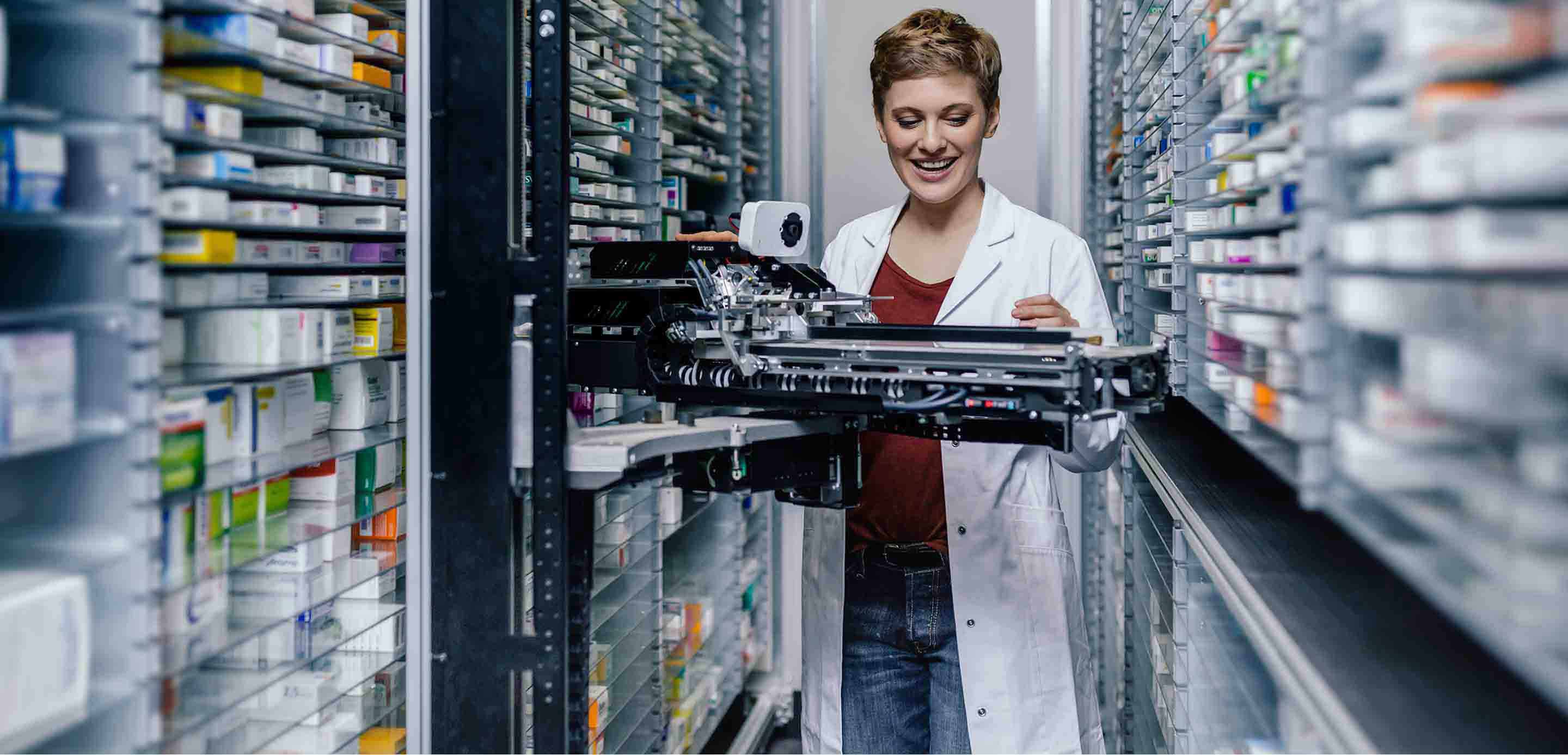 Smiling pharmacist with commissioning machine in pharmacy