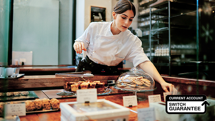 Female baker behind the counter picking up an item to give to a customer