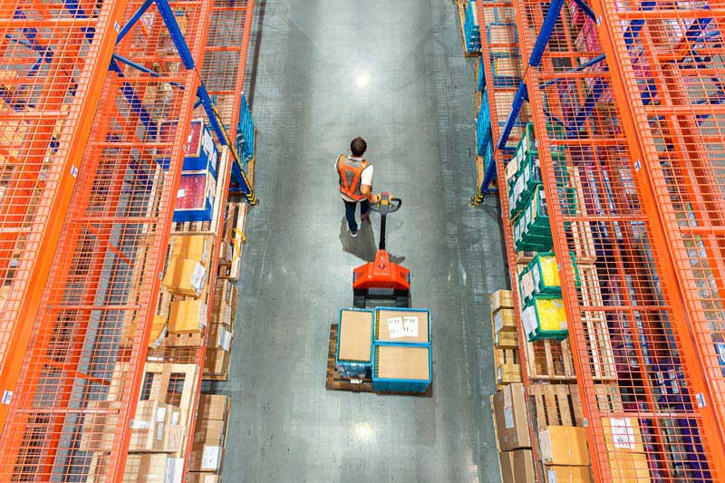 High angle view of warehouse worker pulling a pallet truck at distribution warehouse High angle view of warehouse worker pulling a pallet truck at distribution warehouse